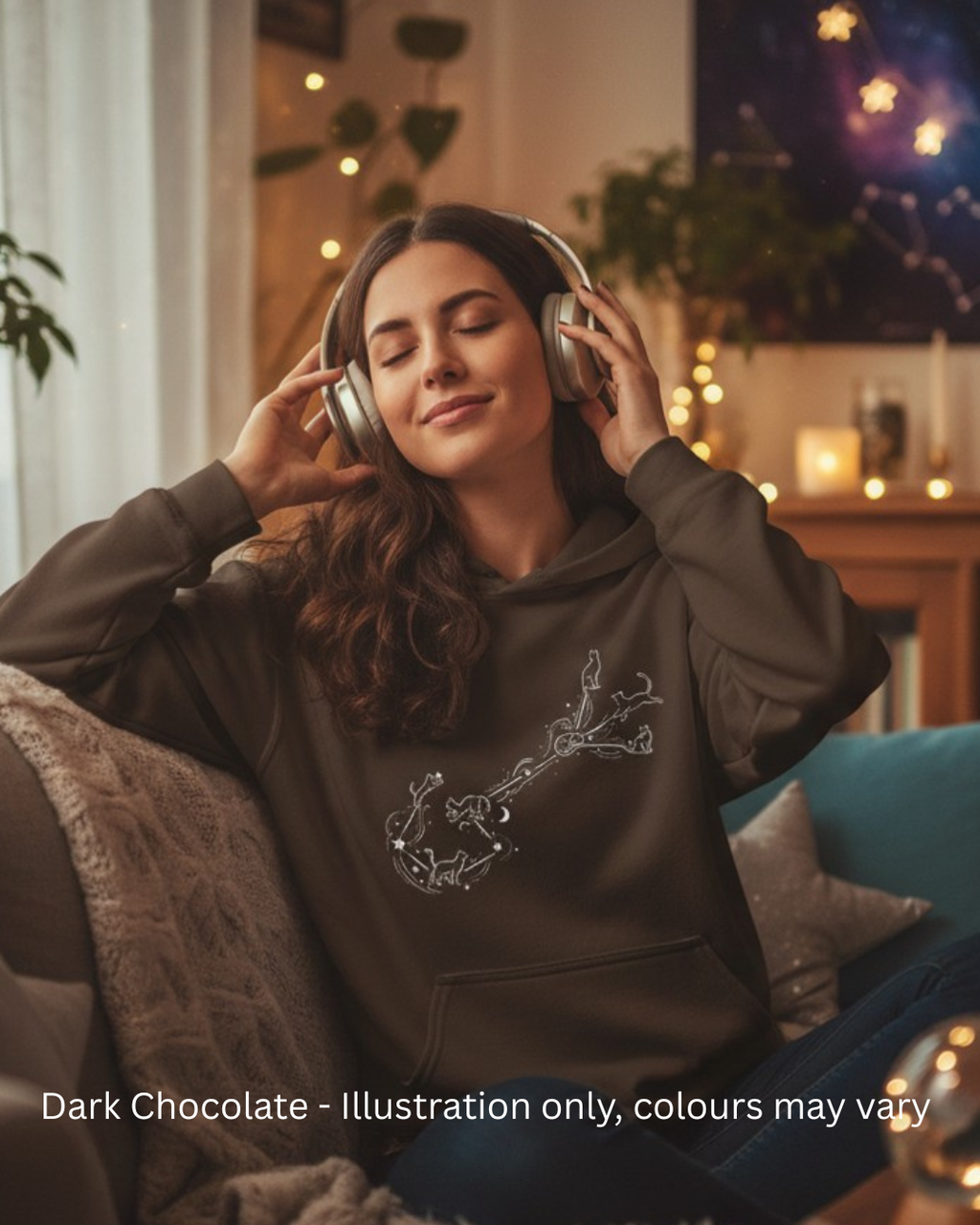 Woman wearing a dark chocolate hoodie with a subtle illustration, sitting on a couch in a cozy room.