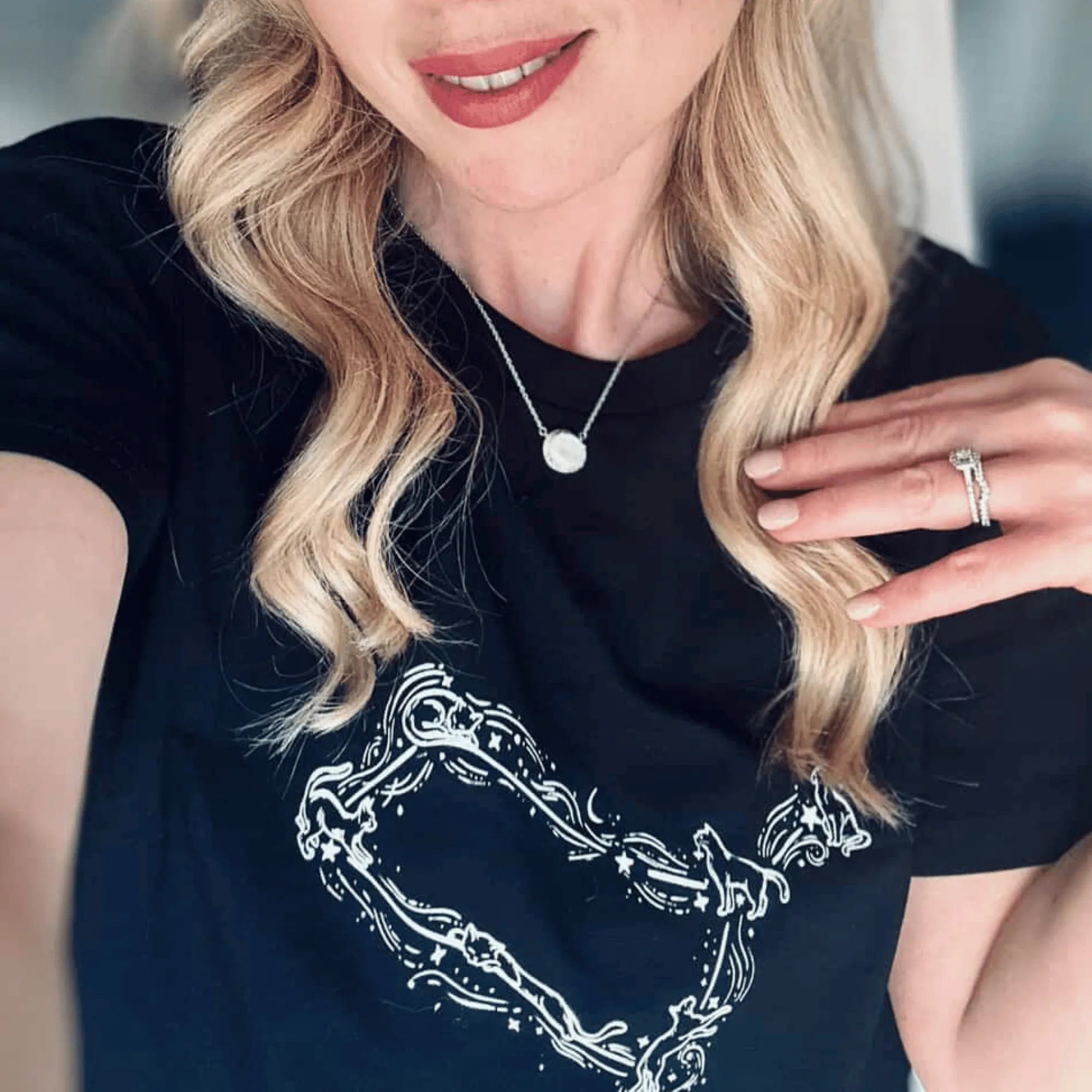 Woman wearing a black t-shirt with a white graphic design, holding her hand near her face.